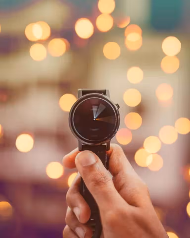 Hand hält eine Smartwatch mit Bokeh-Hintergrund, Fokus auf Zeit.